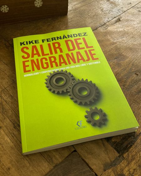 Portada del libro Salir del engranaje, de Kike Fernández, sobre minimalismo y cooperativismo, con tres engranajes sobre fondo verde lima, fotografiado sobre una mesa de madera.